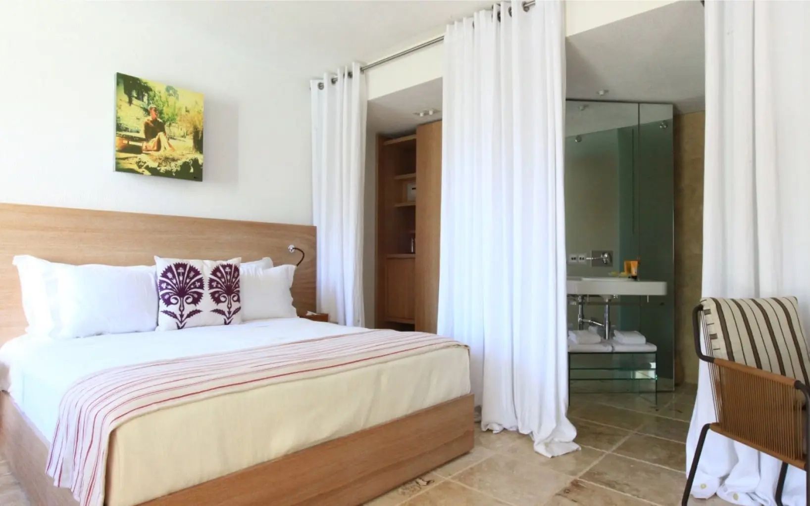 Helles Schlafzimmer mit Doppelbett, weißem Vorhang und Blick auf das Badezimmer.
