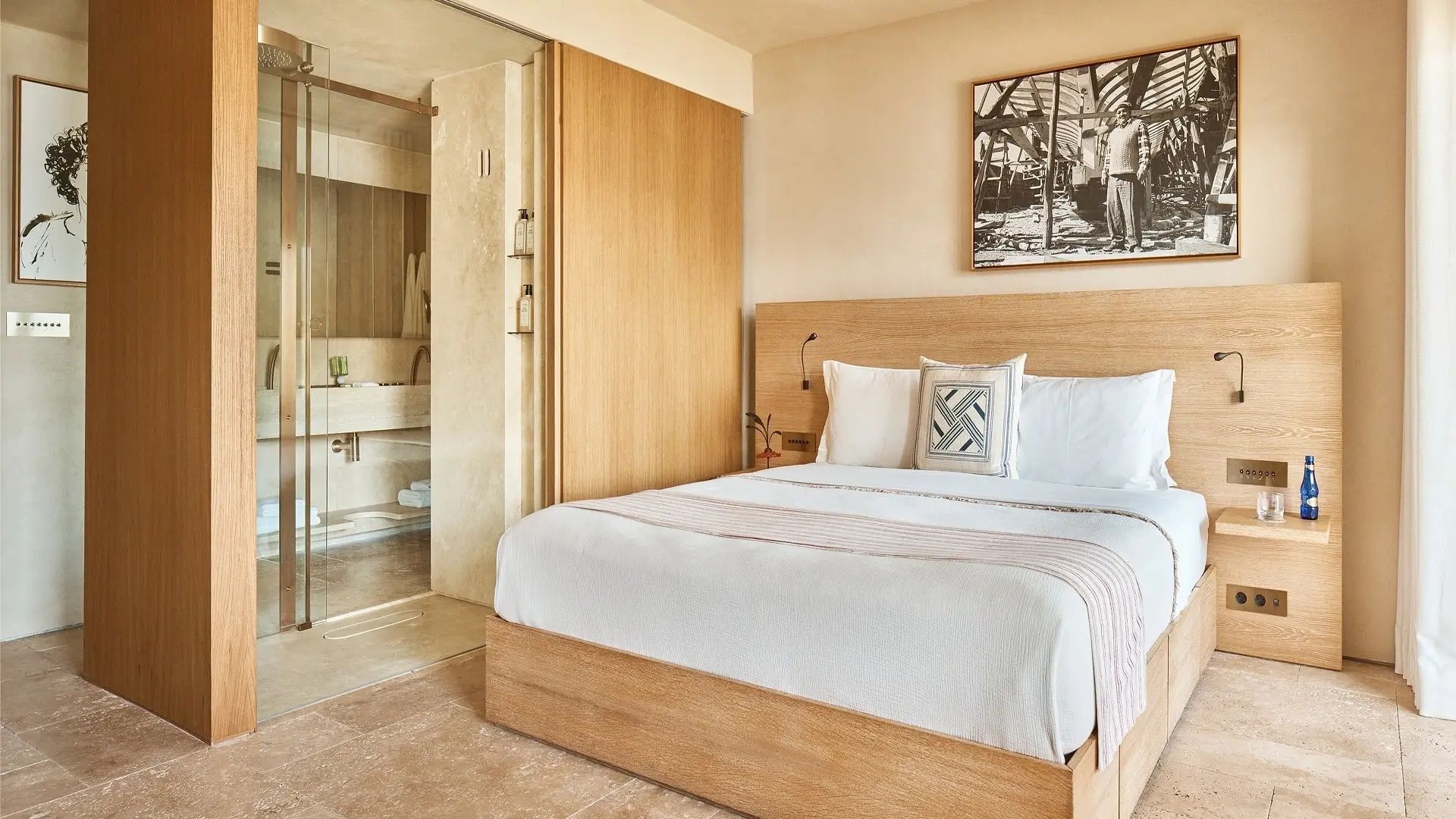 Helles Hotelzimmer mit großem Doppelbett aus Holz und Glaswand zum Badezimmer.