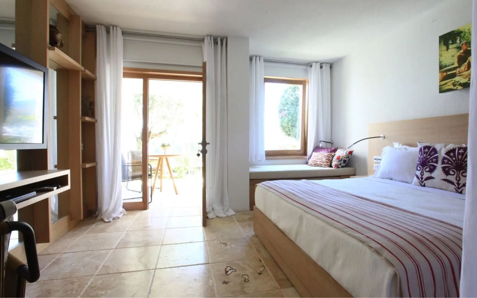 Helles Zimmer mit Fliesenboden, Sitznische am Fenster und Tür zur Terrasse.
