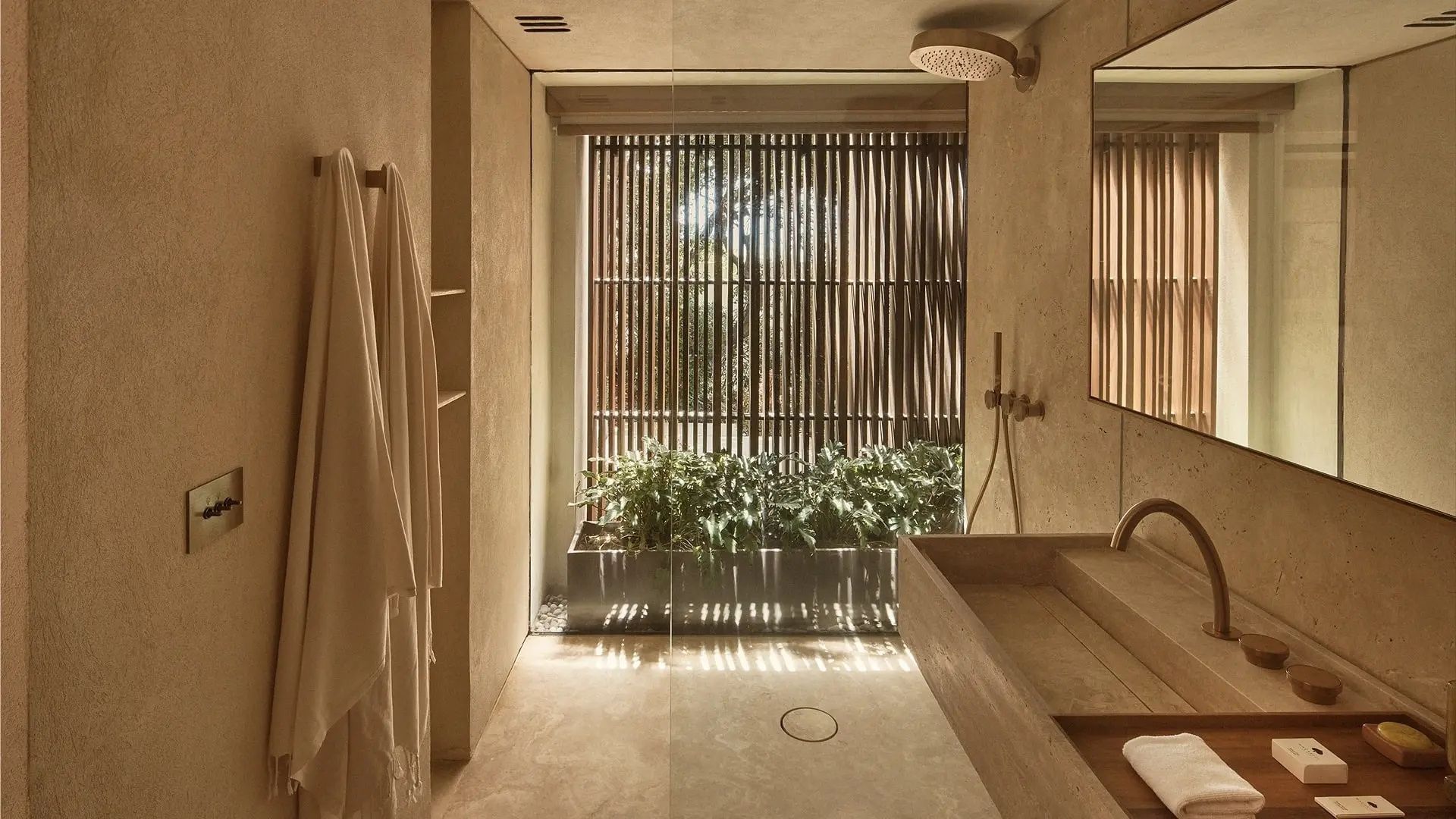 Badezimmer mit bodengleicher Dusche, Holzlamellen, Pflanzen und einem Waschbecken aus Stein.