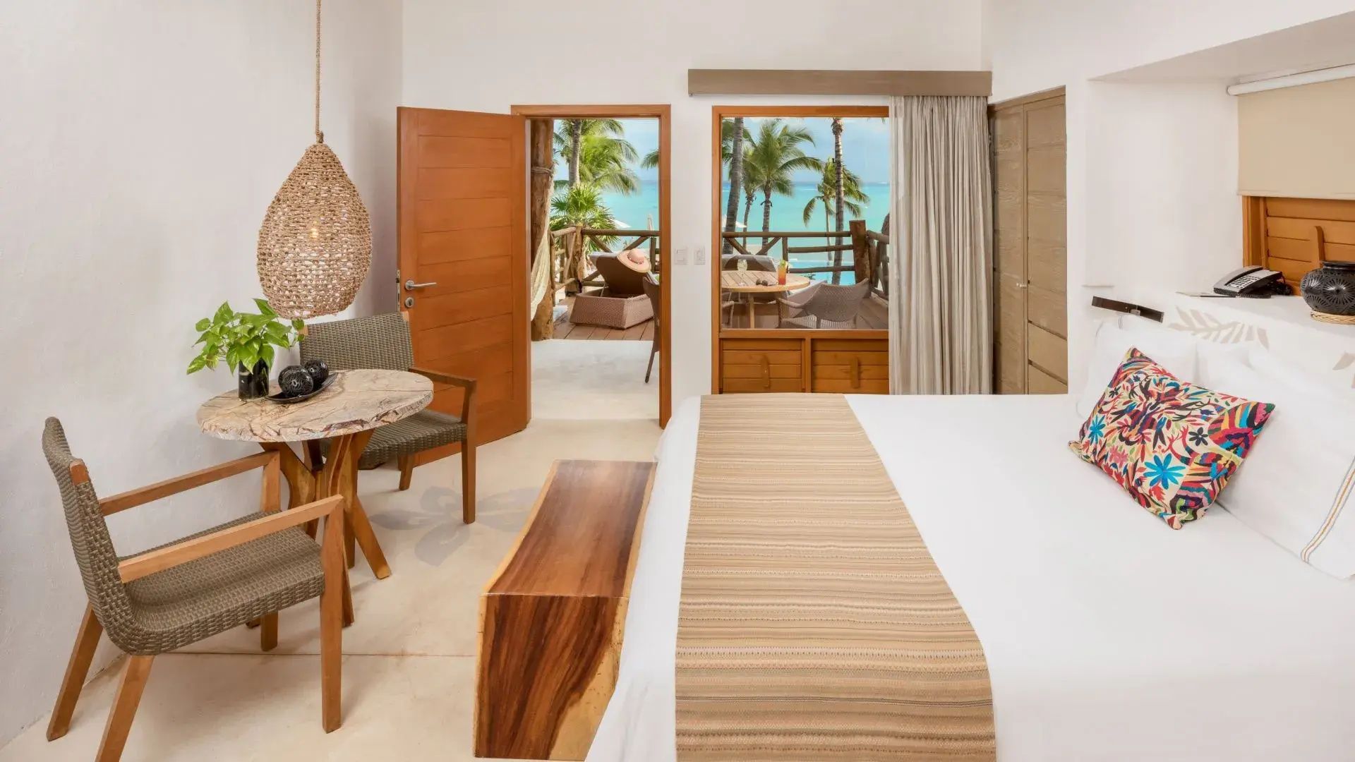Helles Hotelzimmer mit Doppelbett, Holzbank und Blick auf die Terrasse mit Meerblick.