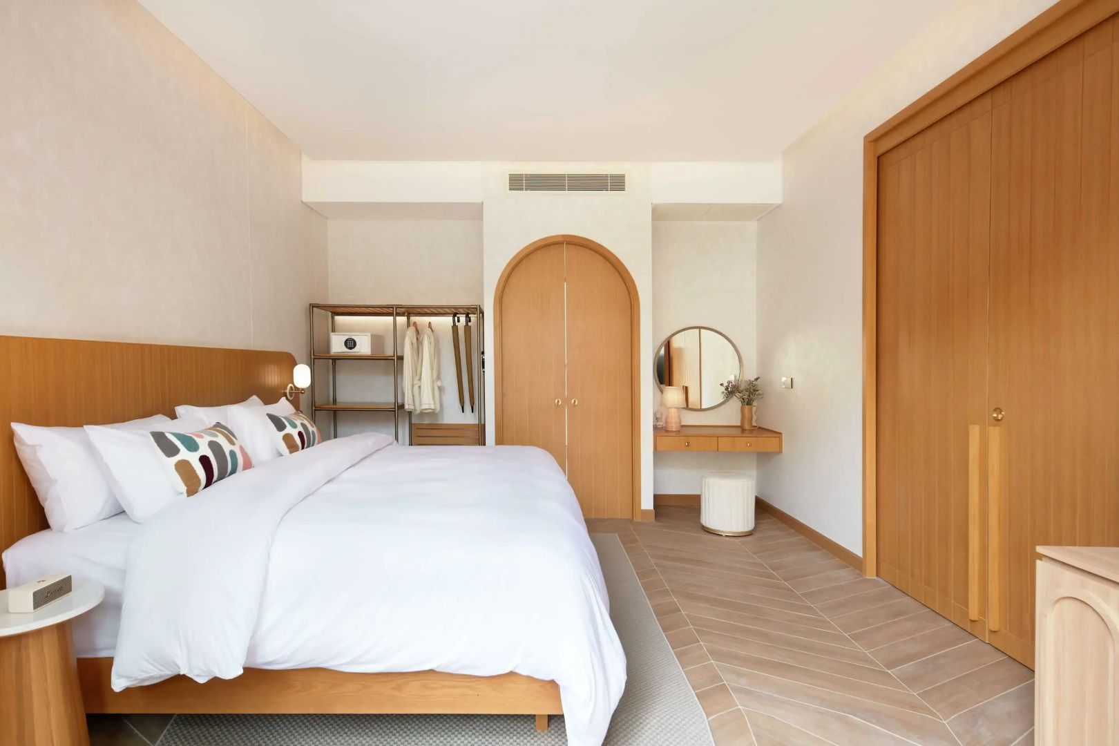 Helles Schlafzimmer mit Doppelbett, Rundbogentür aus Holz, Frisiertisch und Schrank.