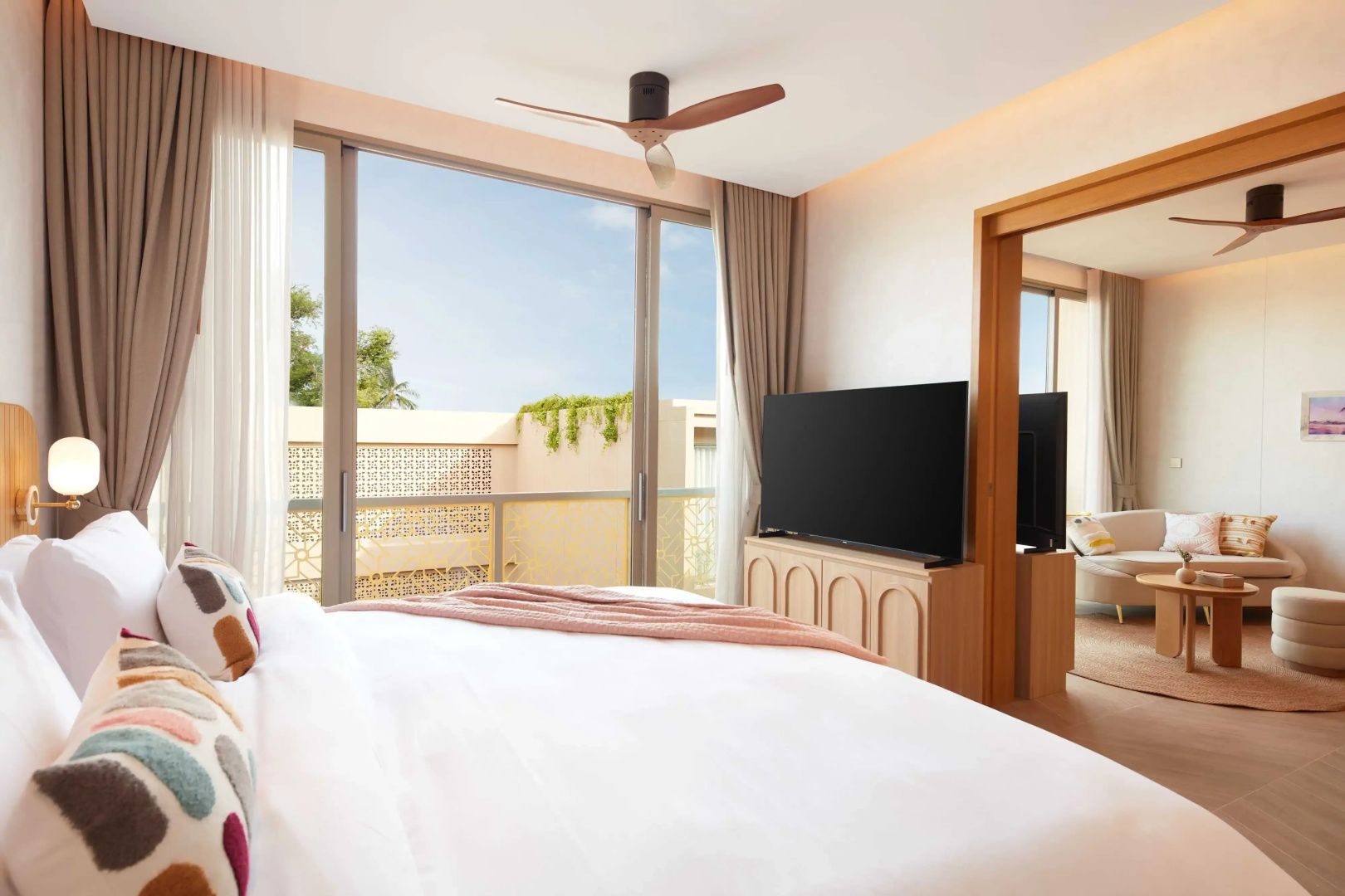 Schlafzimmer mit Fernseher auf Holzkommode, großer Glasfront zum Balkon und Deckenventilator.