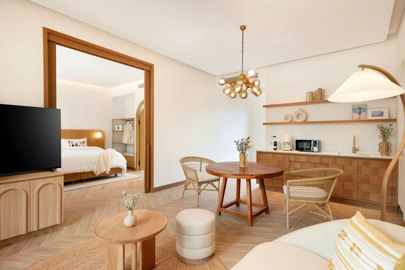 Essbereich mit rundem Holztisch, Korbstühlen, modernem Leuchter und Blick ins Schlafzimmer.