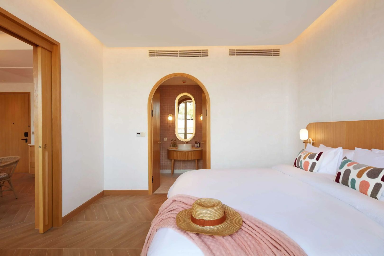 Blick über das Bett mit rosa Decke auf einen Rundbogen mit Durchgang zum Badezimmer.