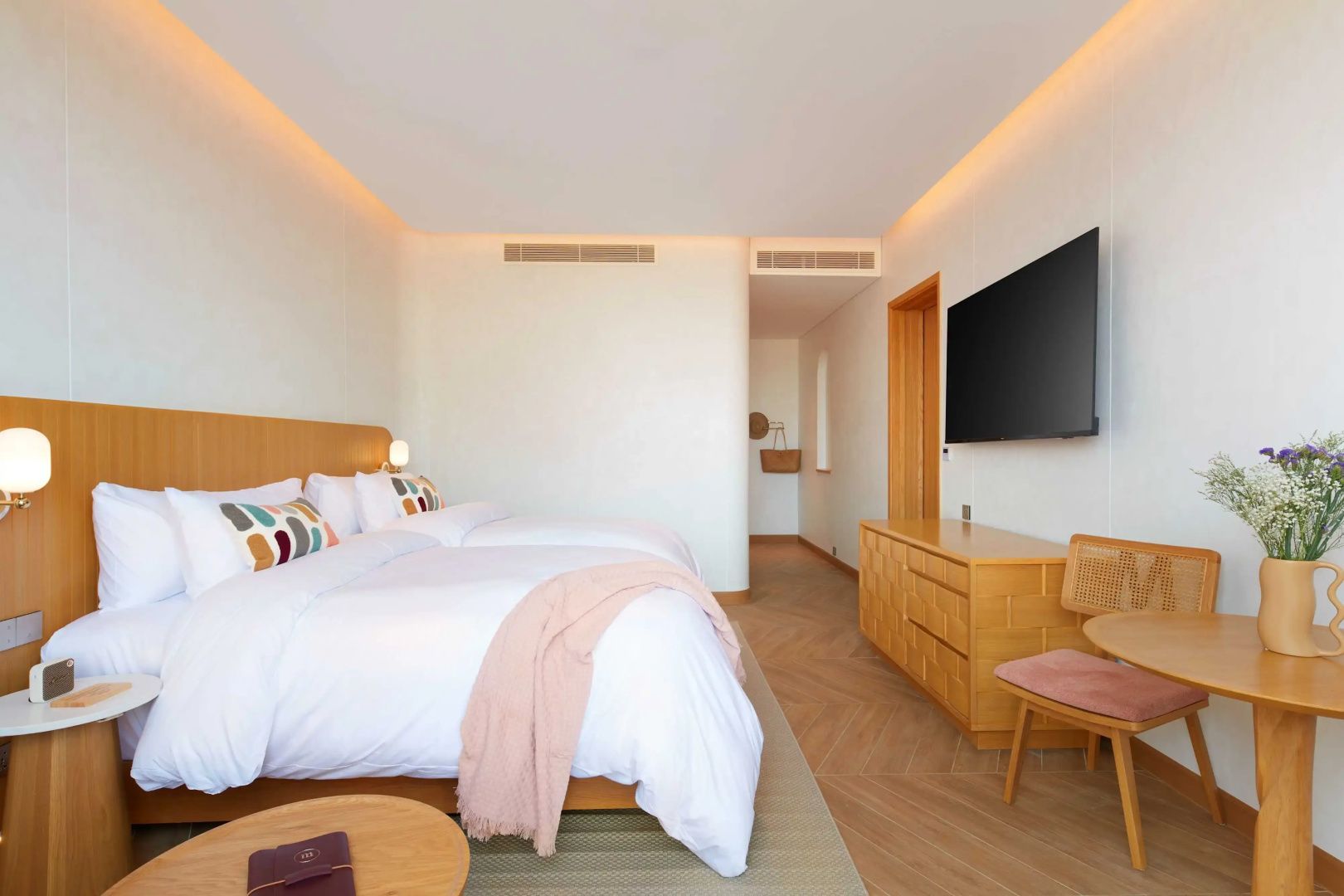 Helles Hotelzimmer mit Doppelbett, Holzmöbeln, Wandfernseher und Parkettboden.