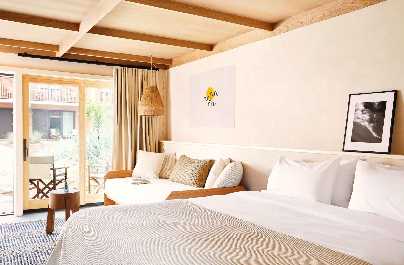 Schlafbereich mit Bett, Tagesbett am Fenster und Deckenbalken aus Holz.