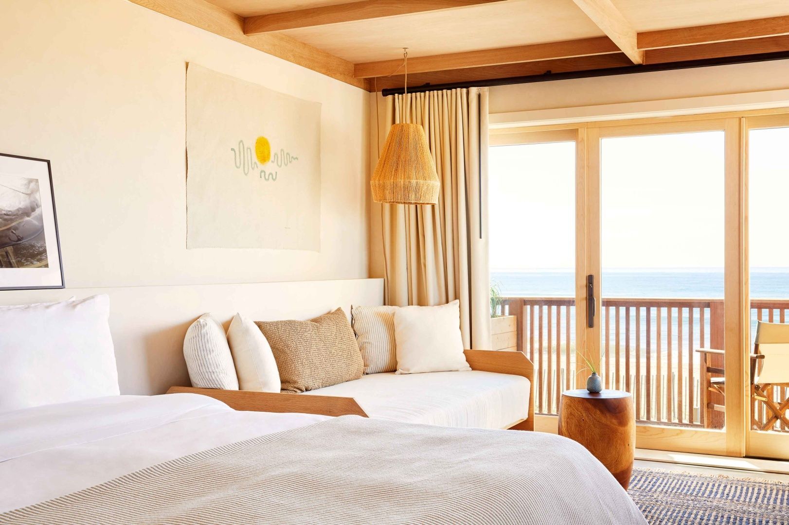 Helles Hotelzimmer mit gemütlichem Tagbett, Flechtlampe und Blick auf das Meer.