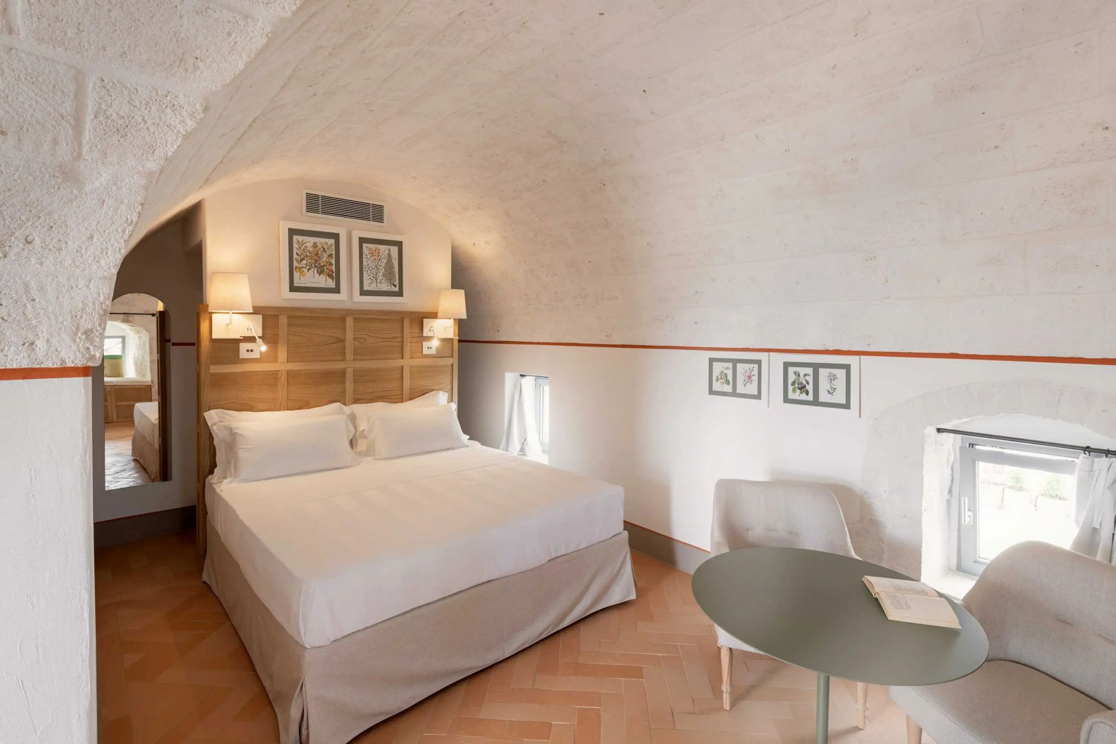 Schlafzimmer mit Tonnengewölbe, weiß bezogenem Doppelbett und einem runden Tisch mit Stuhl.