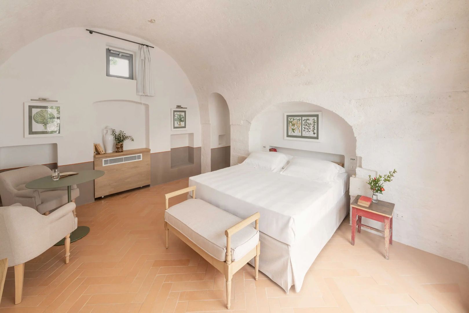 Schlafzimmer mit Doppelbett unter einem weißen Steingewölbe und einer Sitzbank am Fußende.