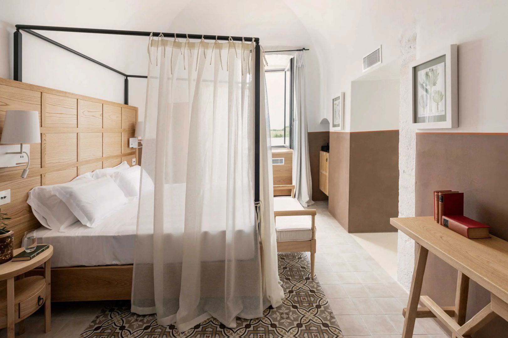 Helles Hotelzimmer mit einem Himmelbett, hellem Vorhang und Fliesenboden unter gewölbter Decke.