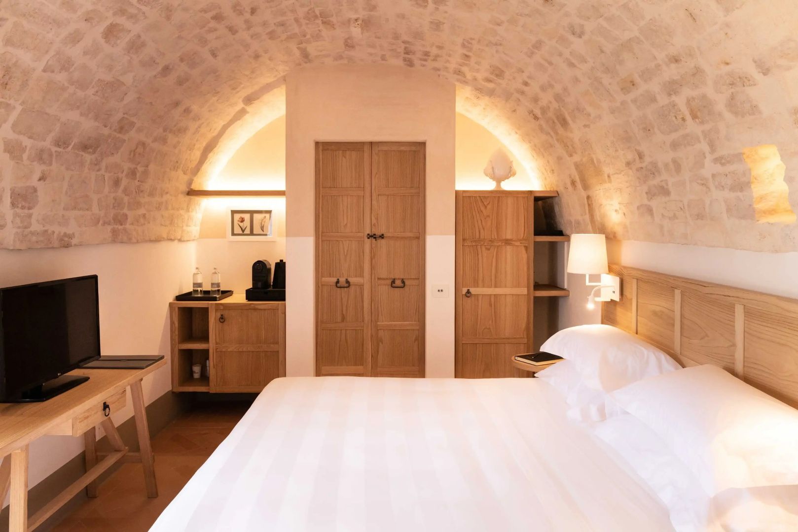 Schlafzimmer mit gewölbter Steindecke, Einbauschränken aus Holz und weiß bezogenem Doppelbett.