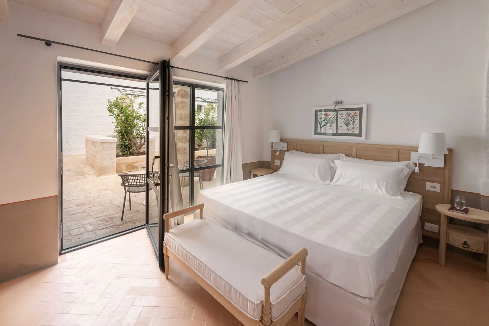 Helles Hotelzimmer mit weißer Holzbalkendecke, Doppelbett und Balkontür zu einem Innenhof.