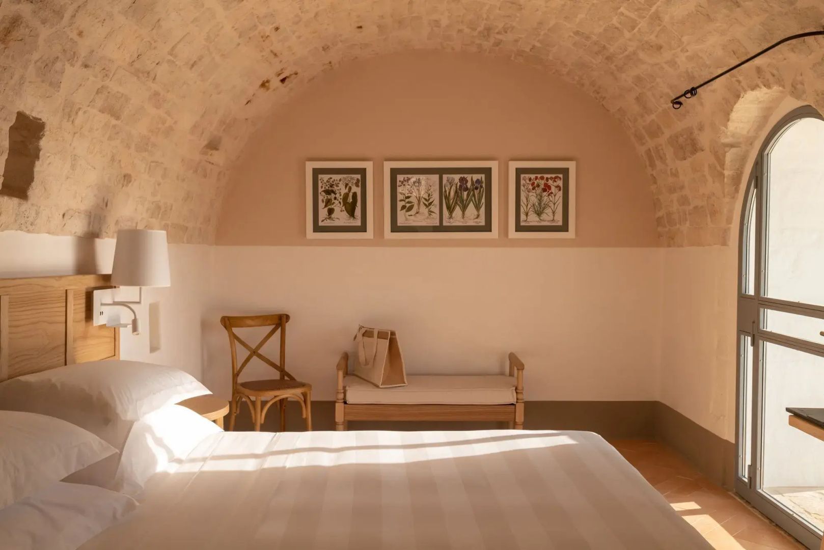 Schlafzimmer mit Tonnengewölbe, Holzmöbeln und botanischen Bildern an der Wand.
