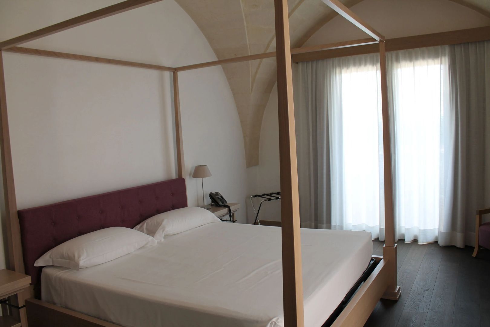 Modernes Himmelbett mit violetter Kopfstütze unter einer historischen Gewölbedecke.