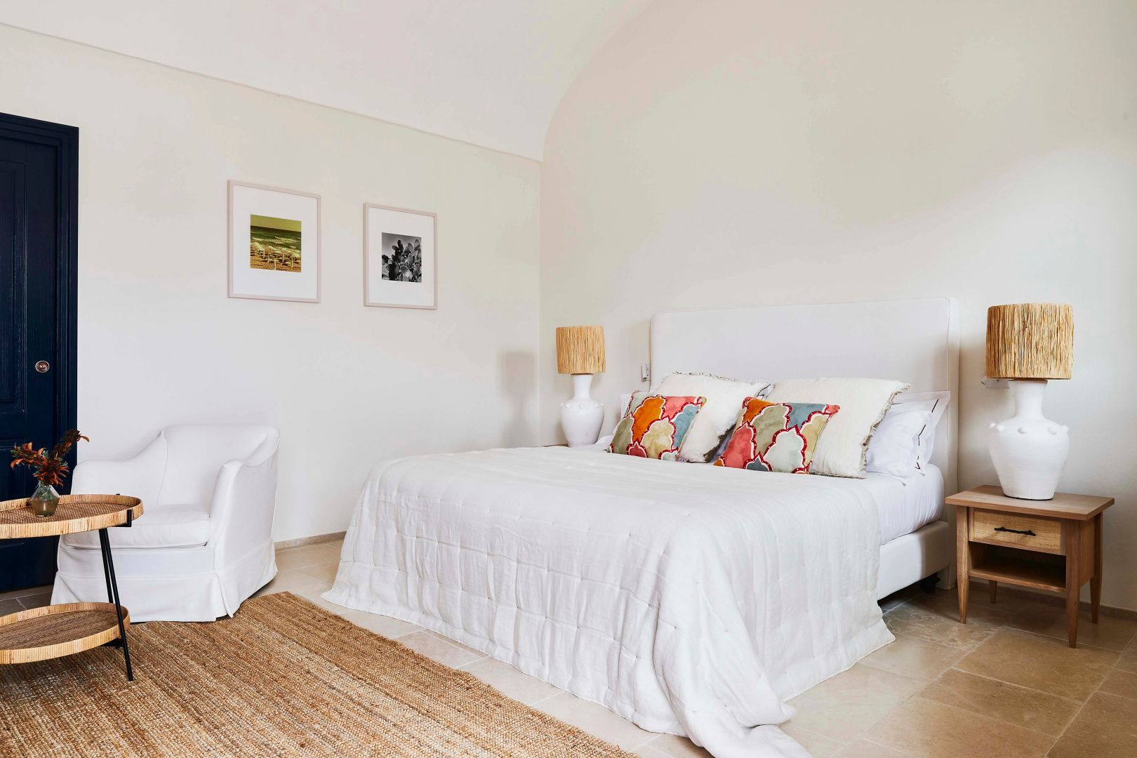 Geräumiges Schlafzimmer mit weiß eingedecktem Doppelbett, bunten Kissen und hellem Steinboden.