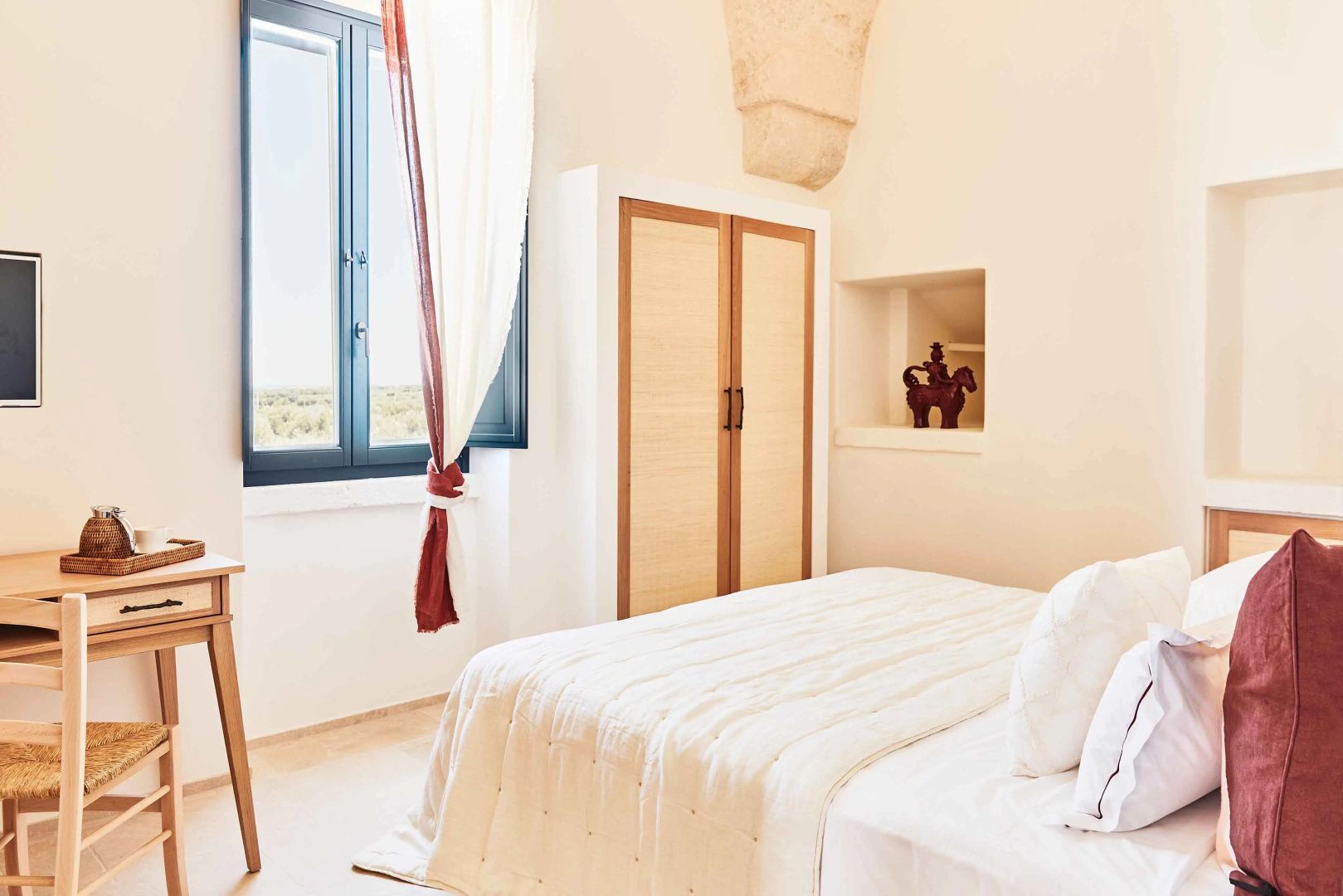 Schlafzimmer mit weißem Bett, Holzschrank und Blick durch das Fenster in die Landschaft.