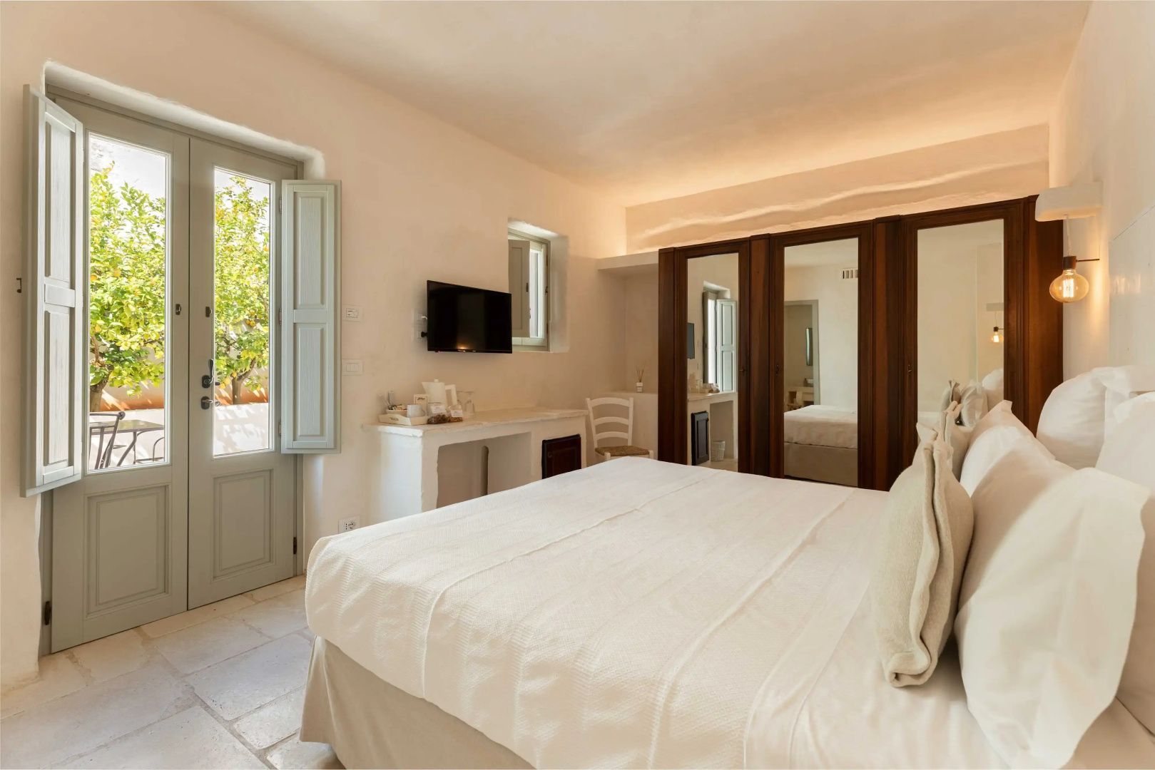 Hell eingerichtetes Hotelzimmer mit Doppelbett, Fernseher und Tür zum Außenbereich.