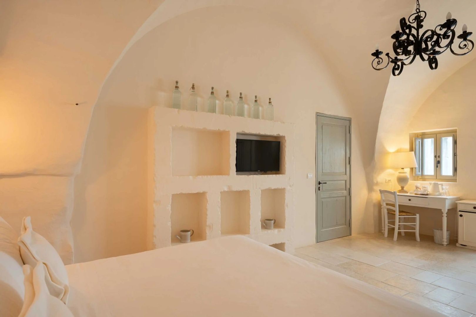 Hell gestaltetes Hotelzimmer mit Gewölbedecke, Wandnische für Fernseher und Glaskrügen.