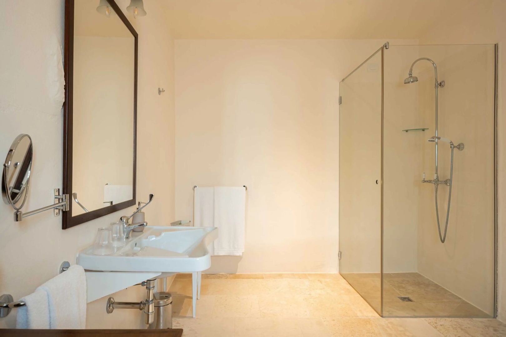 Badezimmer mit weißem Waschbecken, Spiegel und bodengleicher Glasdusche.