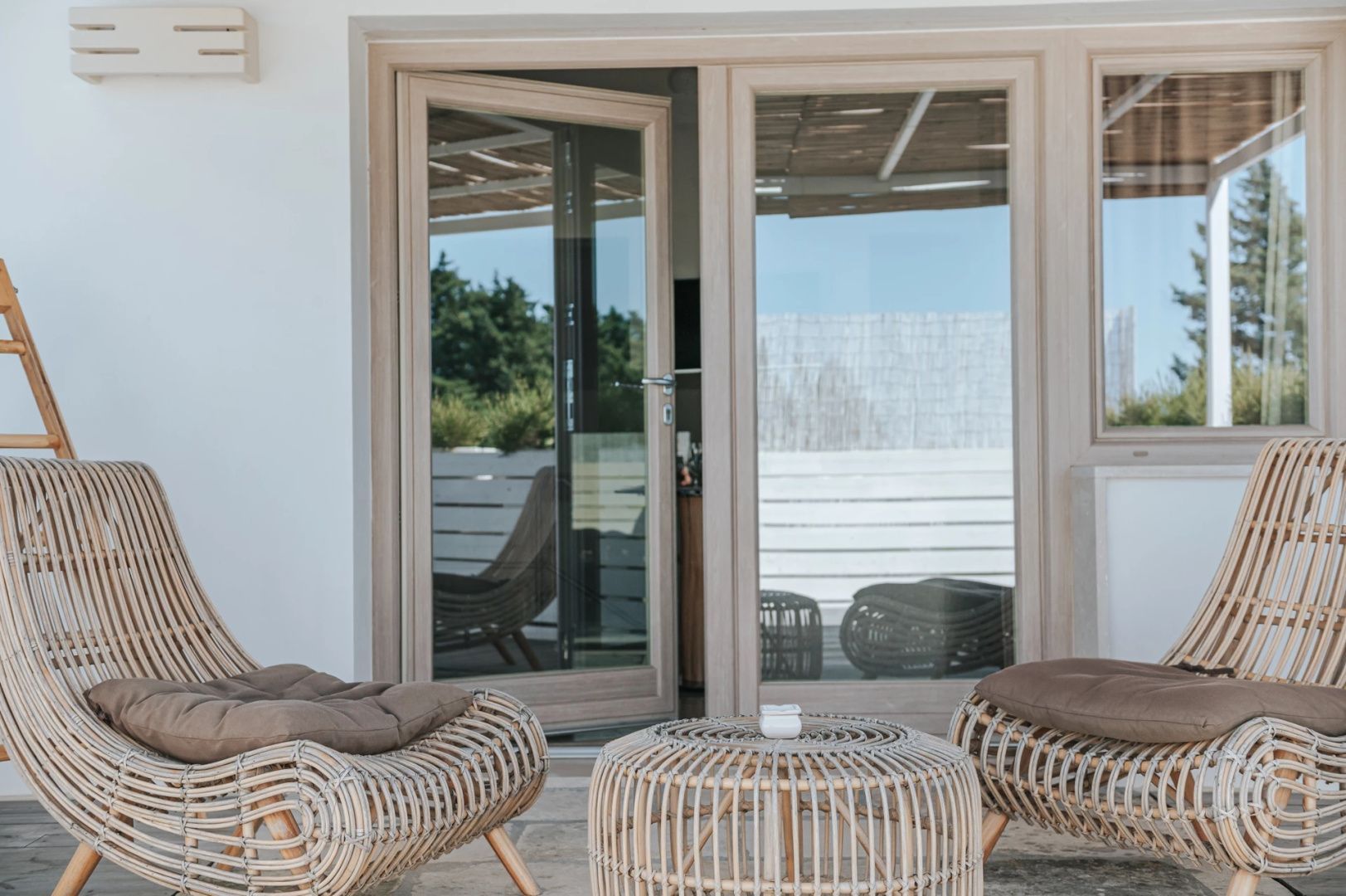 Rattanmöbel auf der Terrasse vor einer Glastür des Hotelgebäudes.