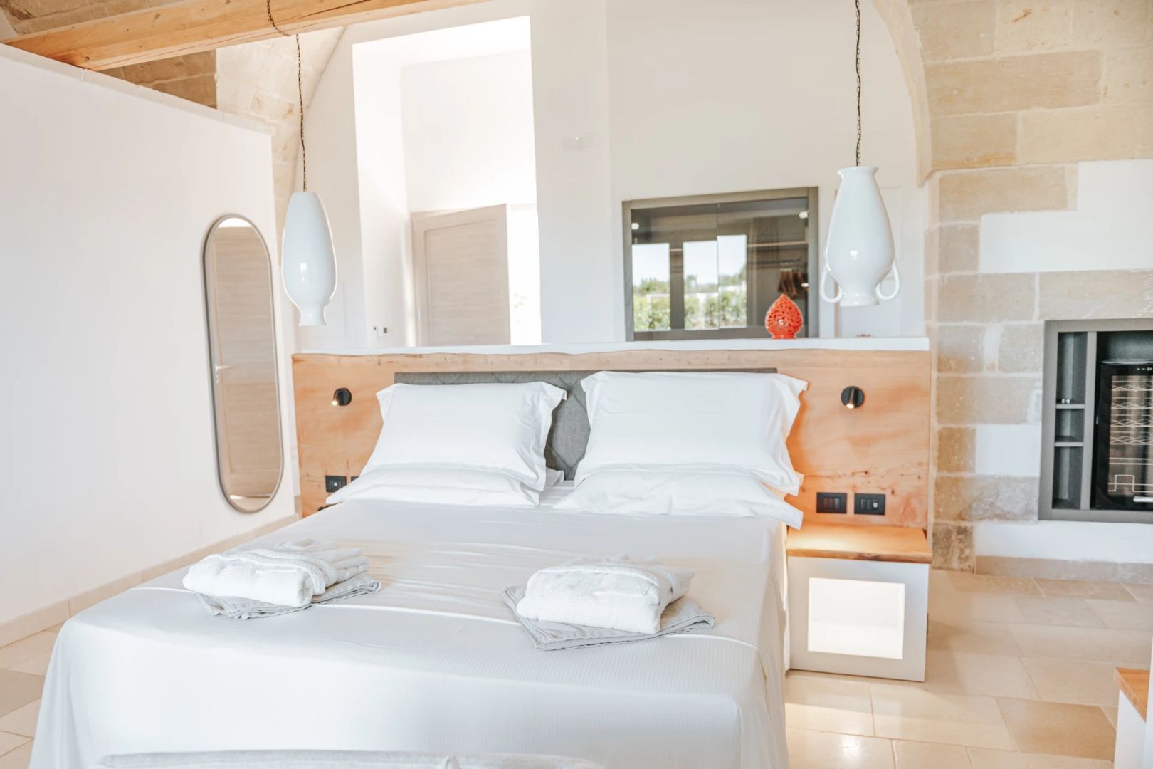 Doppelbett mit weißer Bettwäsche, Kopfteil aus Holz und hängenden Nachttischlampen.