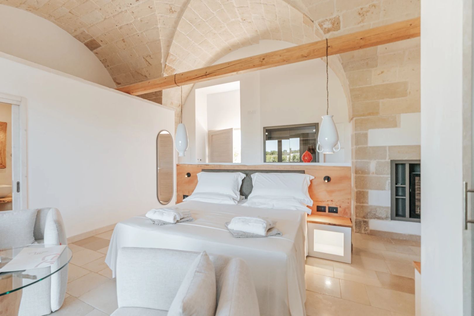 Geräumiges Hotelzimmer mit Natursteindecke, Holzbalken, Doppelbett und Sessel.