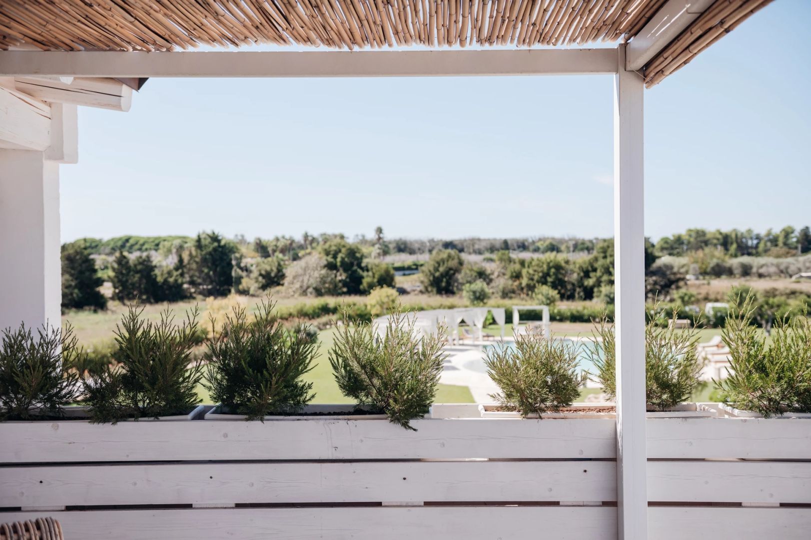 Blick von der überdachten Terrasse auf die grüne Landschaft und den Poolbereich.