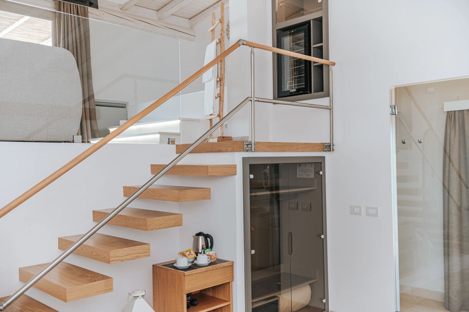 Holztreppe mit Glasgeländer und kleiner Minibar auf Holzschrank in einem Hotelzimmer.