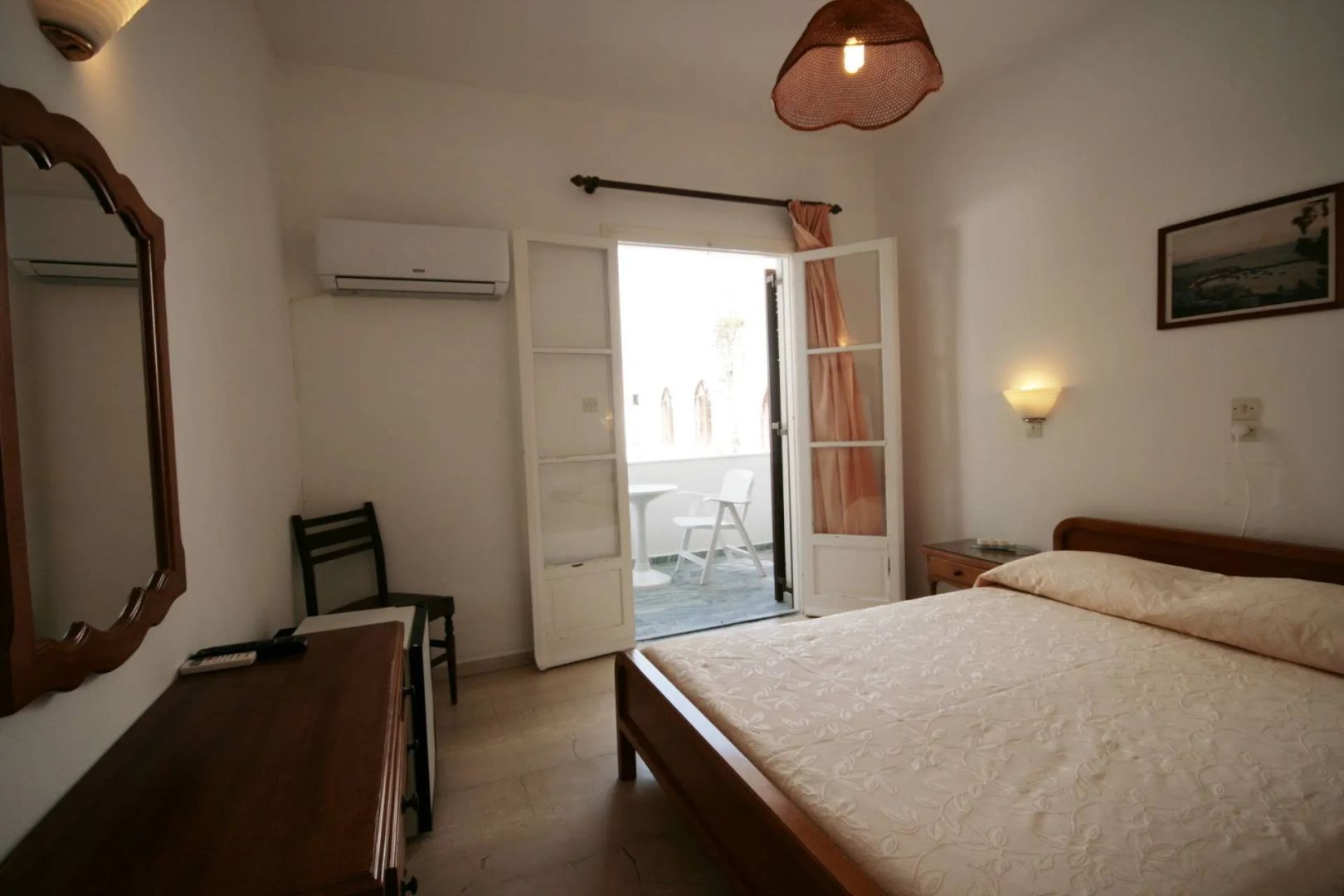 Schlafzimmer mit Doppelbett und geöffneter Balkontür zu einer möblierten Terrasse.