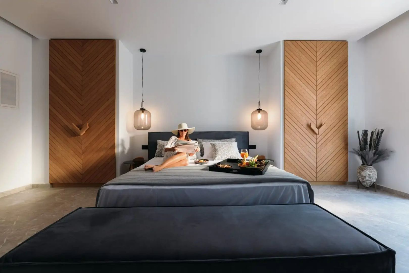 Doppelbett im Schlafzimmer mit Holzelementen und einer Frau beim Frühstück auf dem Bett.