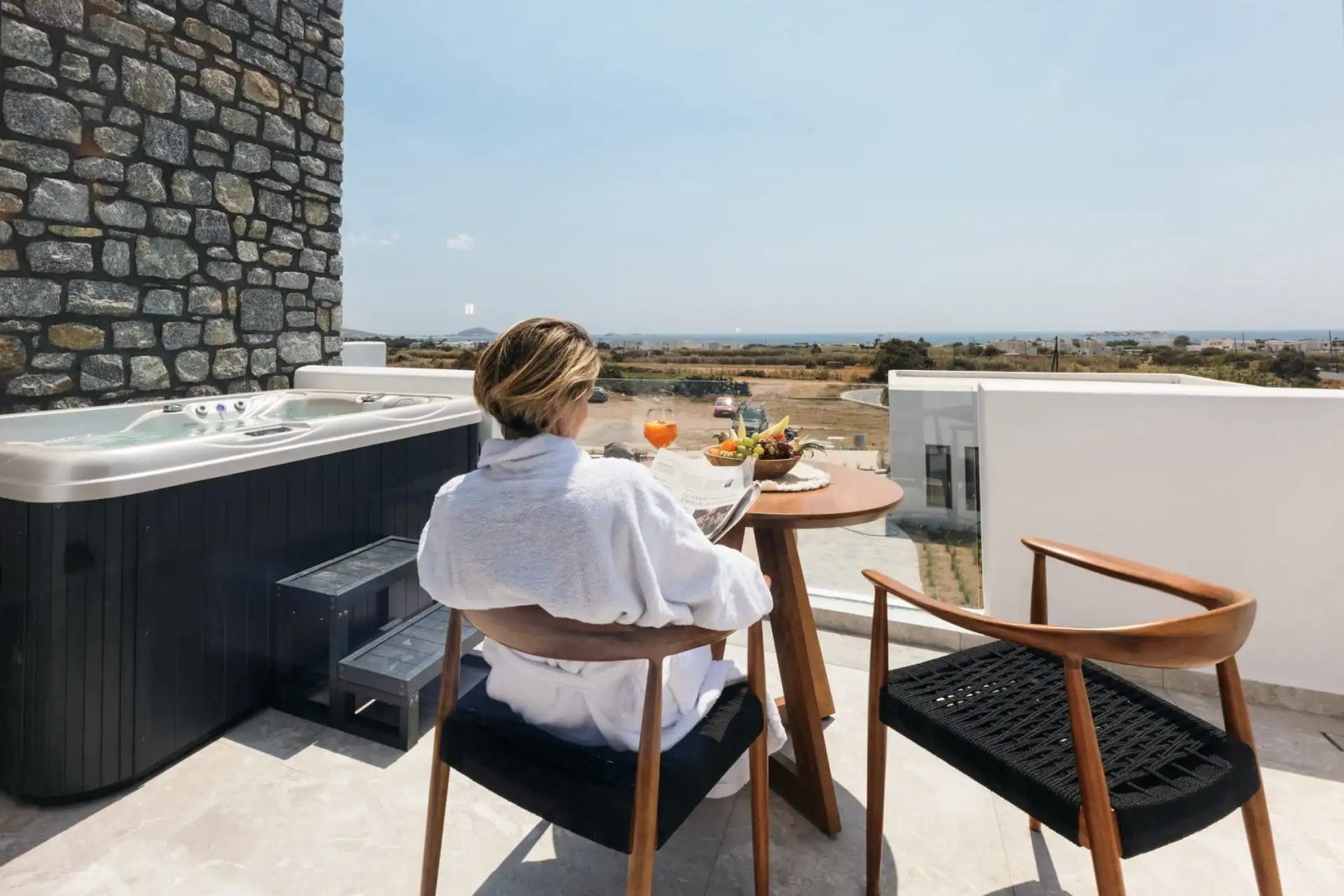 Frau im Bademantel sitzt auf einer Terrasse und blickt auf die Landschaft.