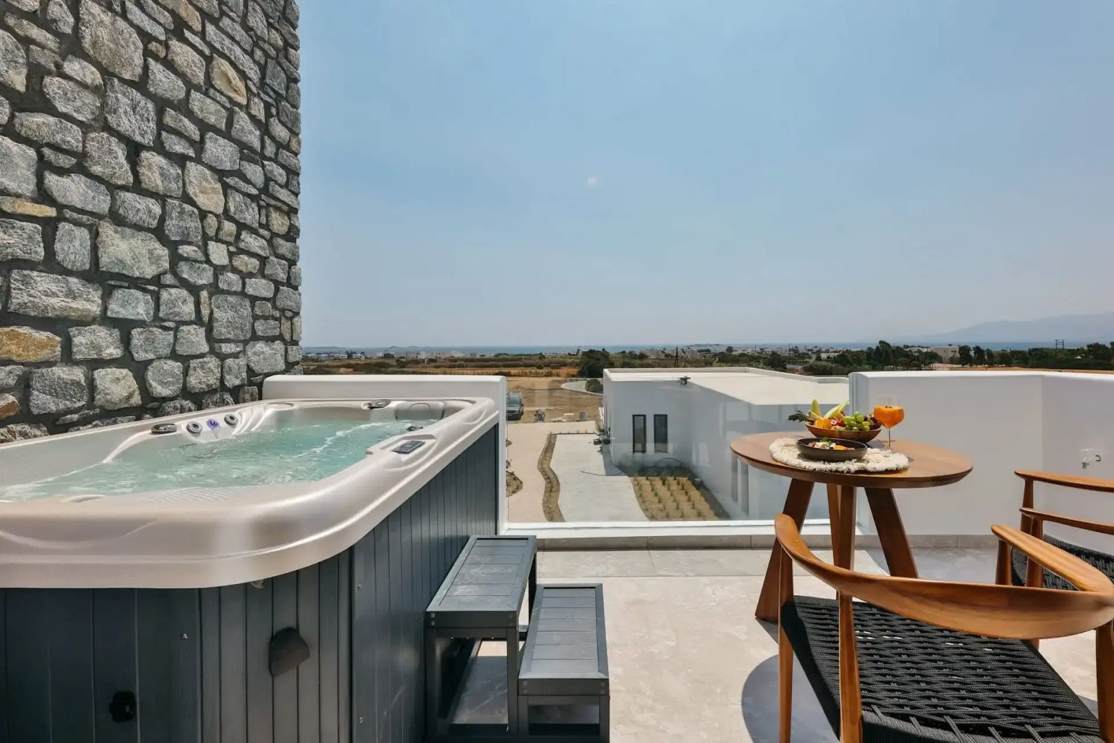 Terrasse mit Whirlpool, Holztisch, Stühlen und Weitblick auf die umliegende Landschaft.
