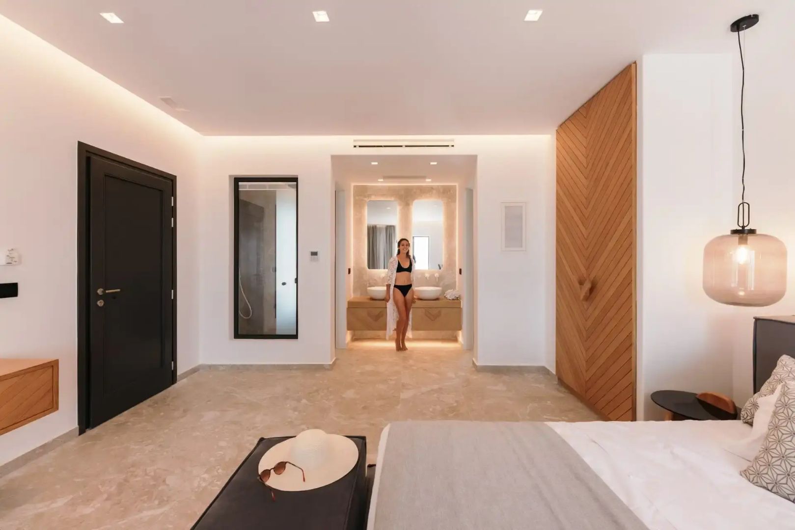 Großes Hotelzimmer mit hellem Fliesenboden, Holzelementen und Blick zum Badezimmer.