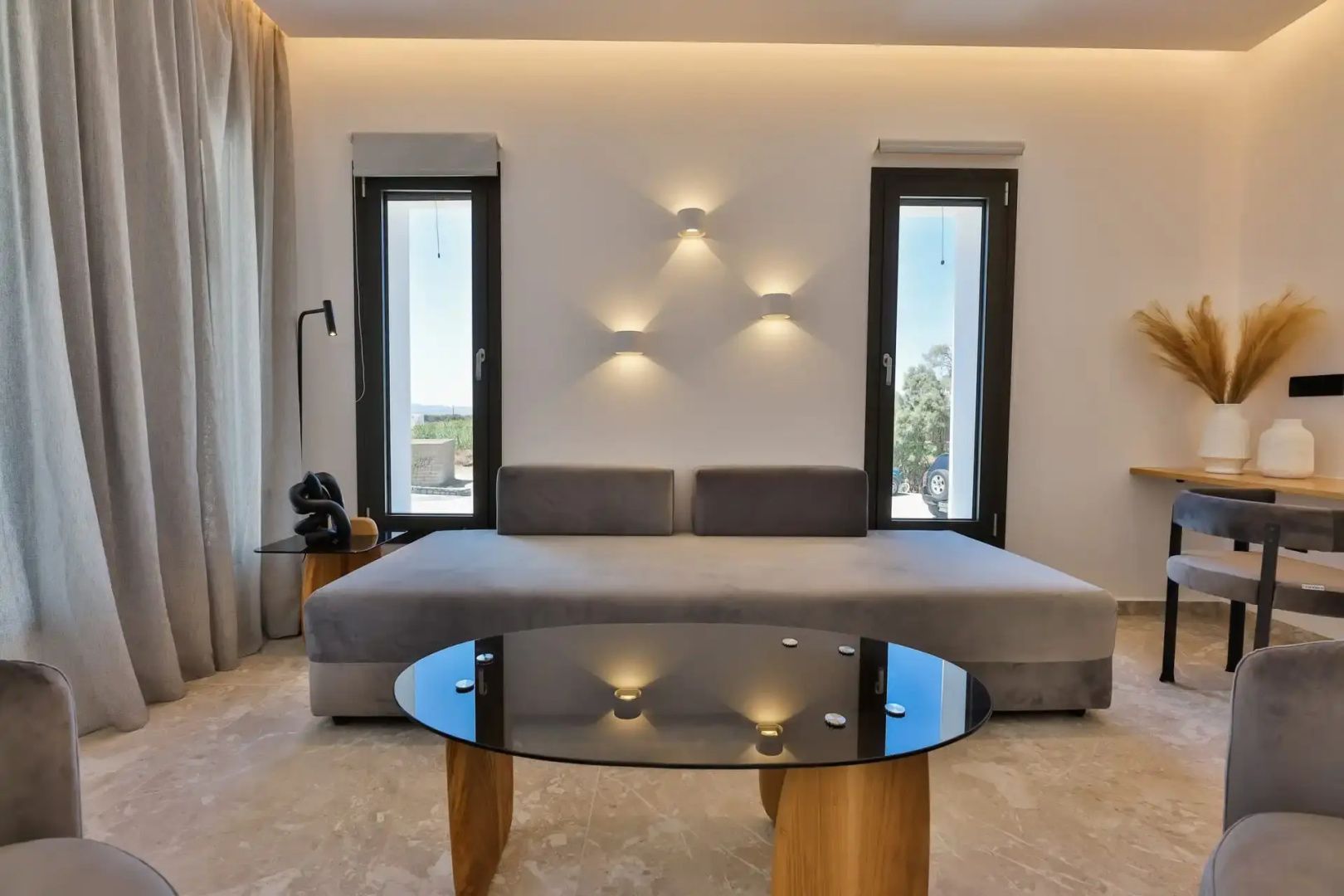 Helles Wohnzimmer mit einem grauen Tagesbett, dunklem Couchtisch und moderner Wandbeleuchtung.