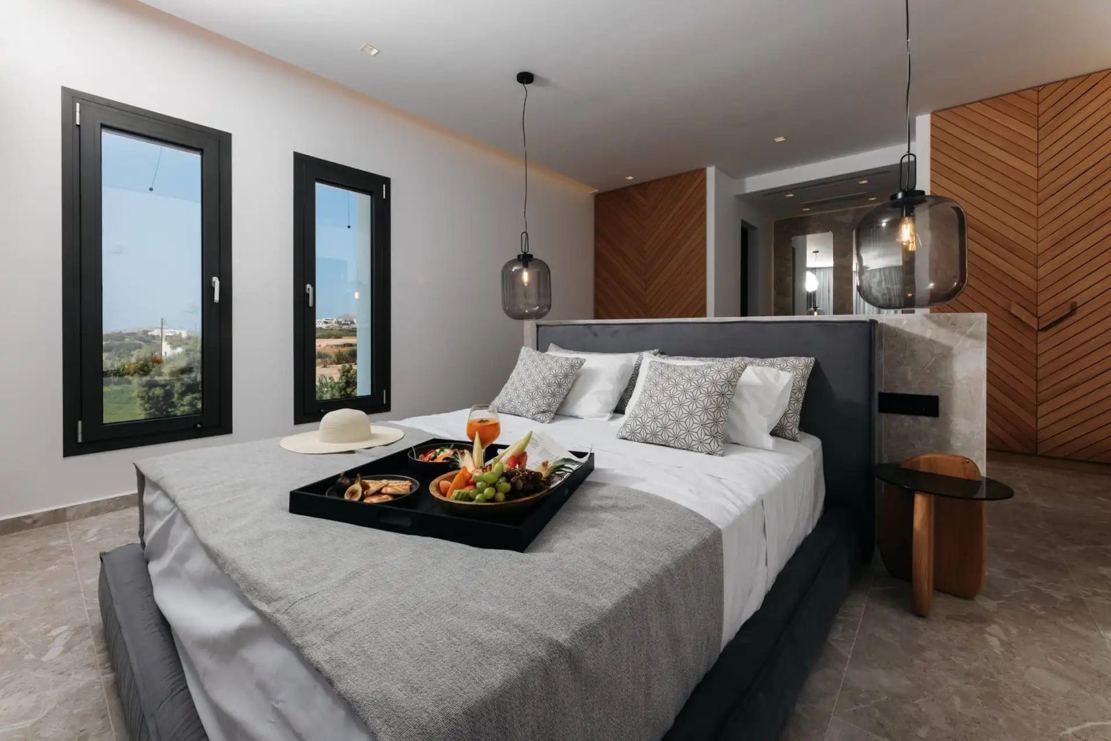 Doppelbett mit grauem Kopfteil, Tablett mit Snacks und zwei stilvollen Hängeleuchten.