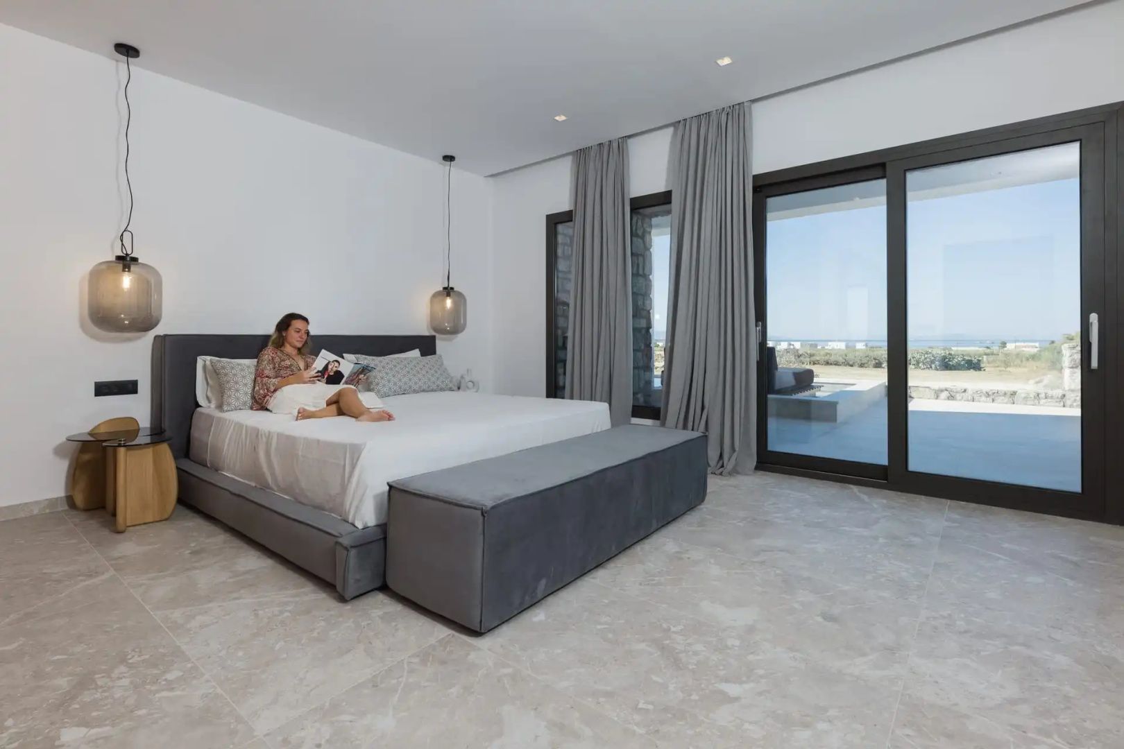 Schlafzimmer mit Doppelbett, gepolsterter Bank und großen Schiebetüren zur Terrasse.