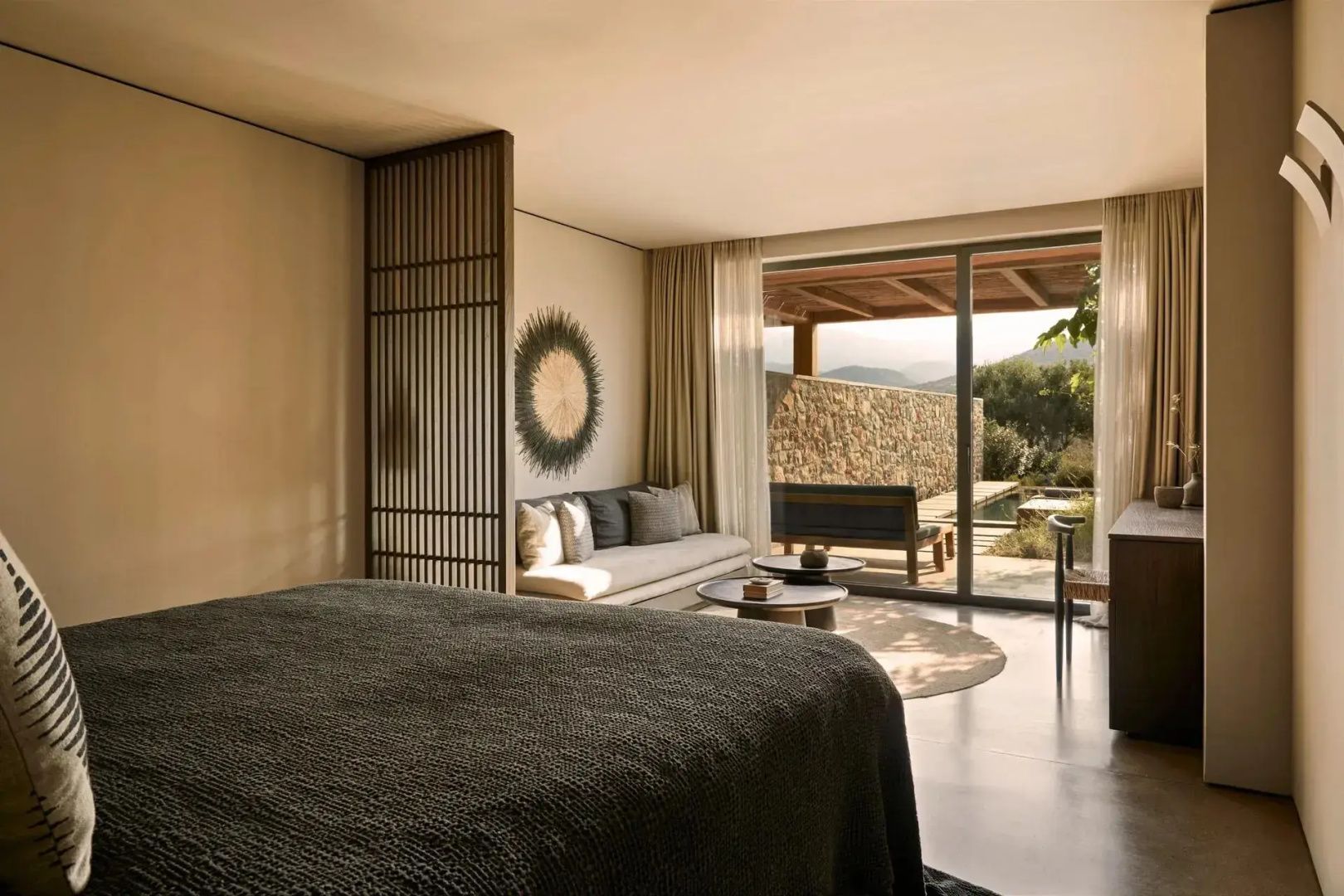 Hotelzimmer mit Bett im Vordergrund, Sofa und Glasschiebetür mit Blick nach draußen.