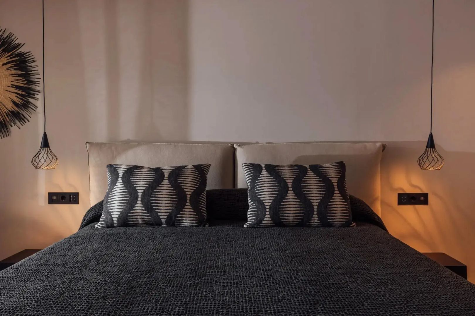 Doppelbett mit dunkler Tagesdecke und zwei gemusterten Kissen vor hellem Kopfteil