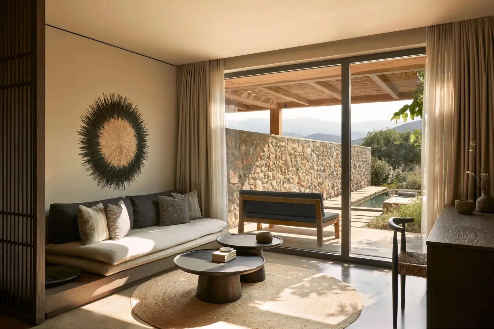 Sitzbereich im Zimmer mit hellem Sofa, Holzdekor und großer Fensterfront zur Terrasse.
