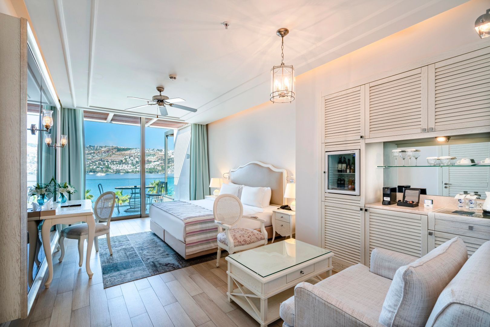 Helles Hotelzimmer mit Doppelbett, Sitzbereich und Balkon mit Blick auf das Meer.