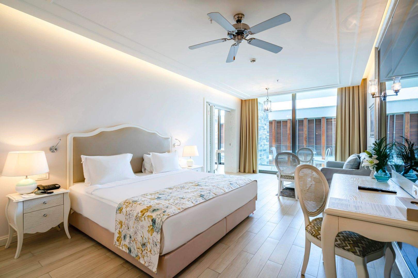 Hell eingerichtetes Schlafzimmer mit Doppelbett, Deckenventilator und Zugang zum Balkon.