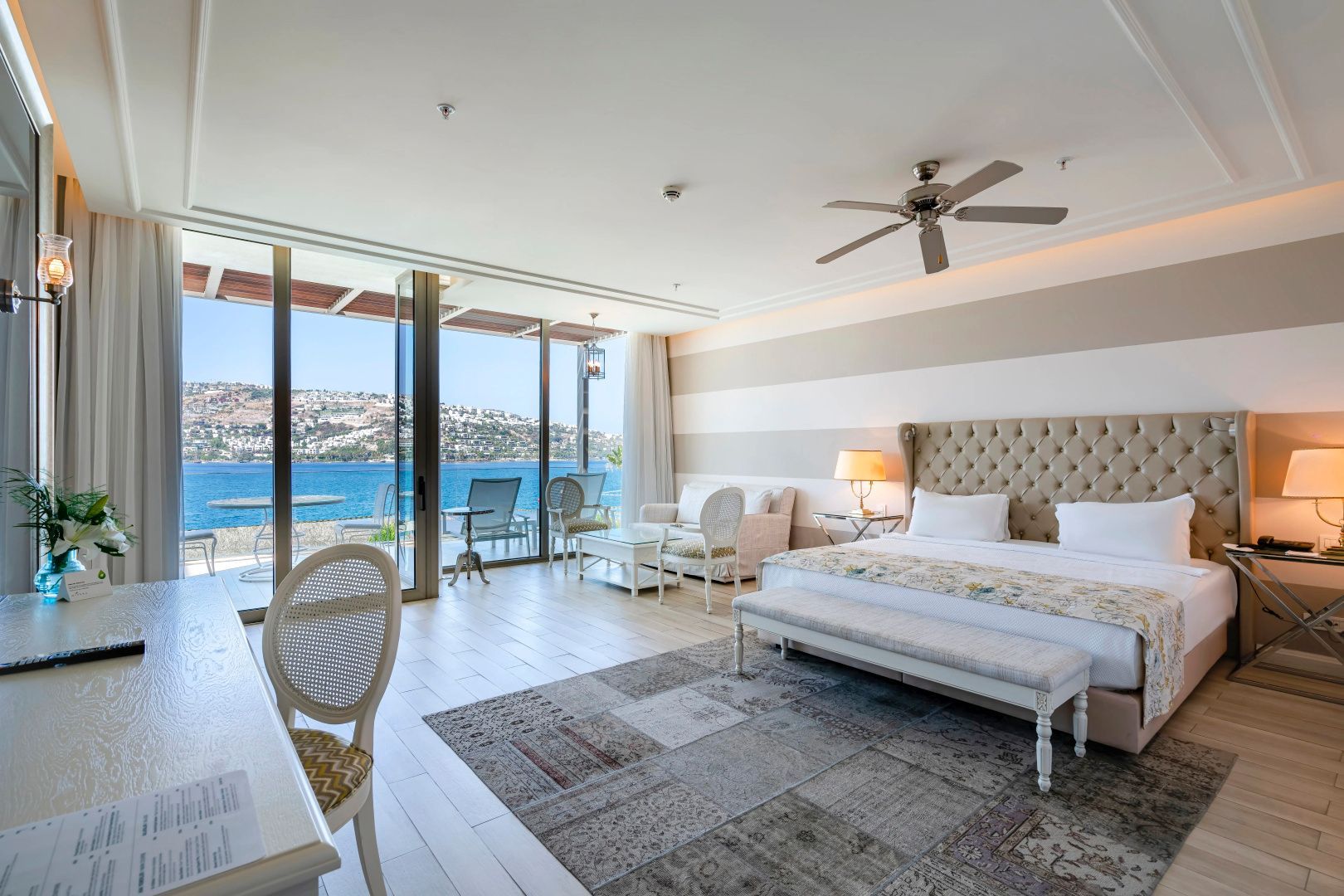 Helles Hotelzimmer mit Doppelbett, Sitzbereich und großer Glasfront mit Blick auf das Meer.