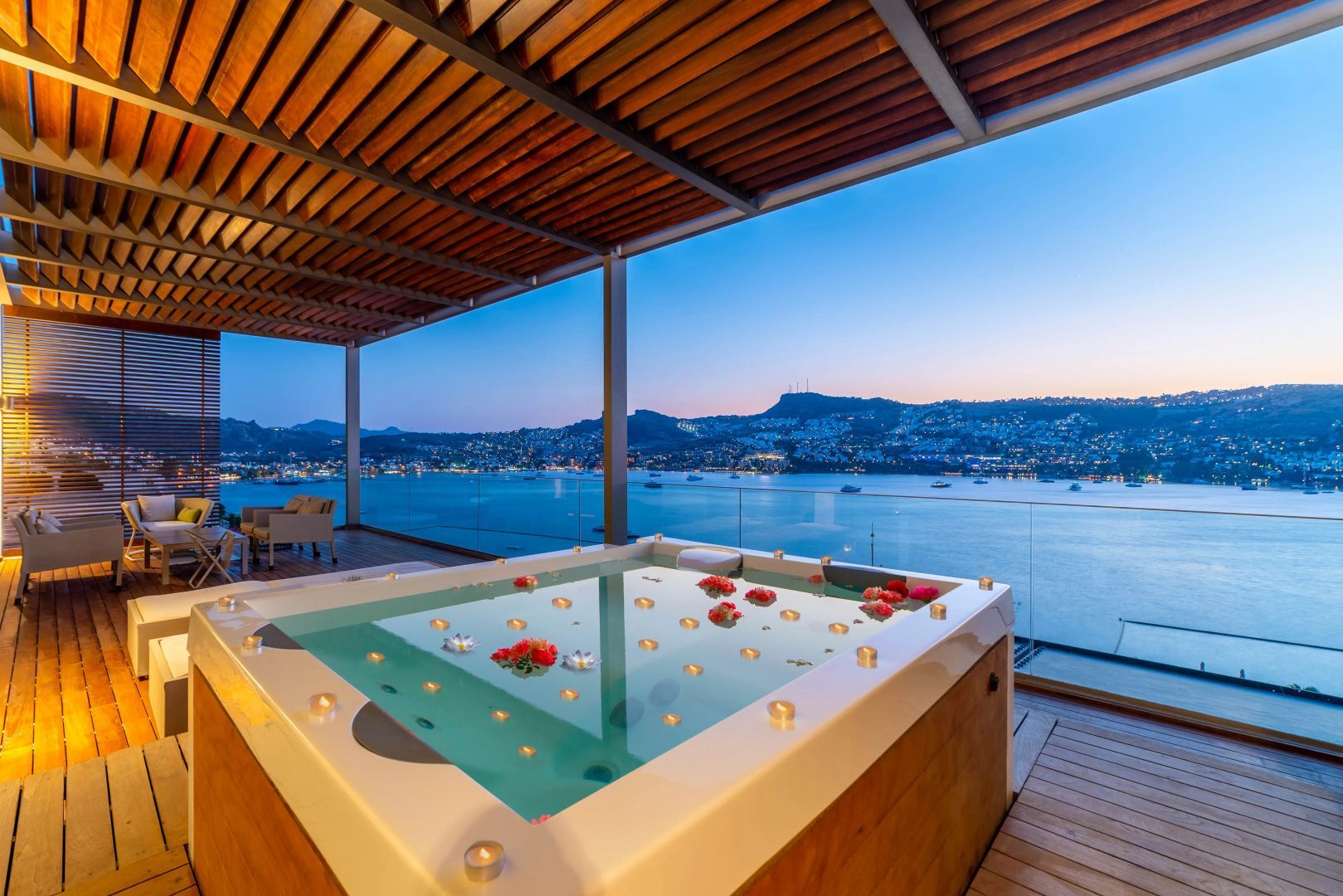 Whirlpool auf der überdachten Terrasse mit Kerzen und Blick auf das Meer bei Dämmerung.