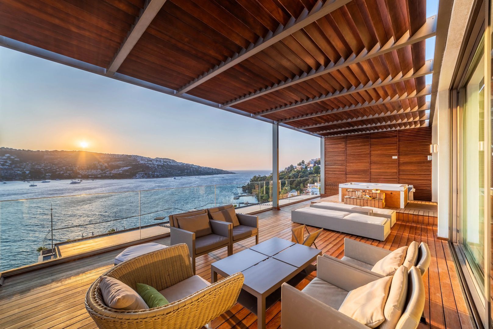 Terrasse mit Holzdeck, Sitzmöbeln und Panoramablick auf die Küste im Sonnenuntergang.