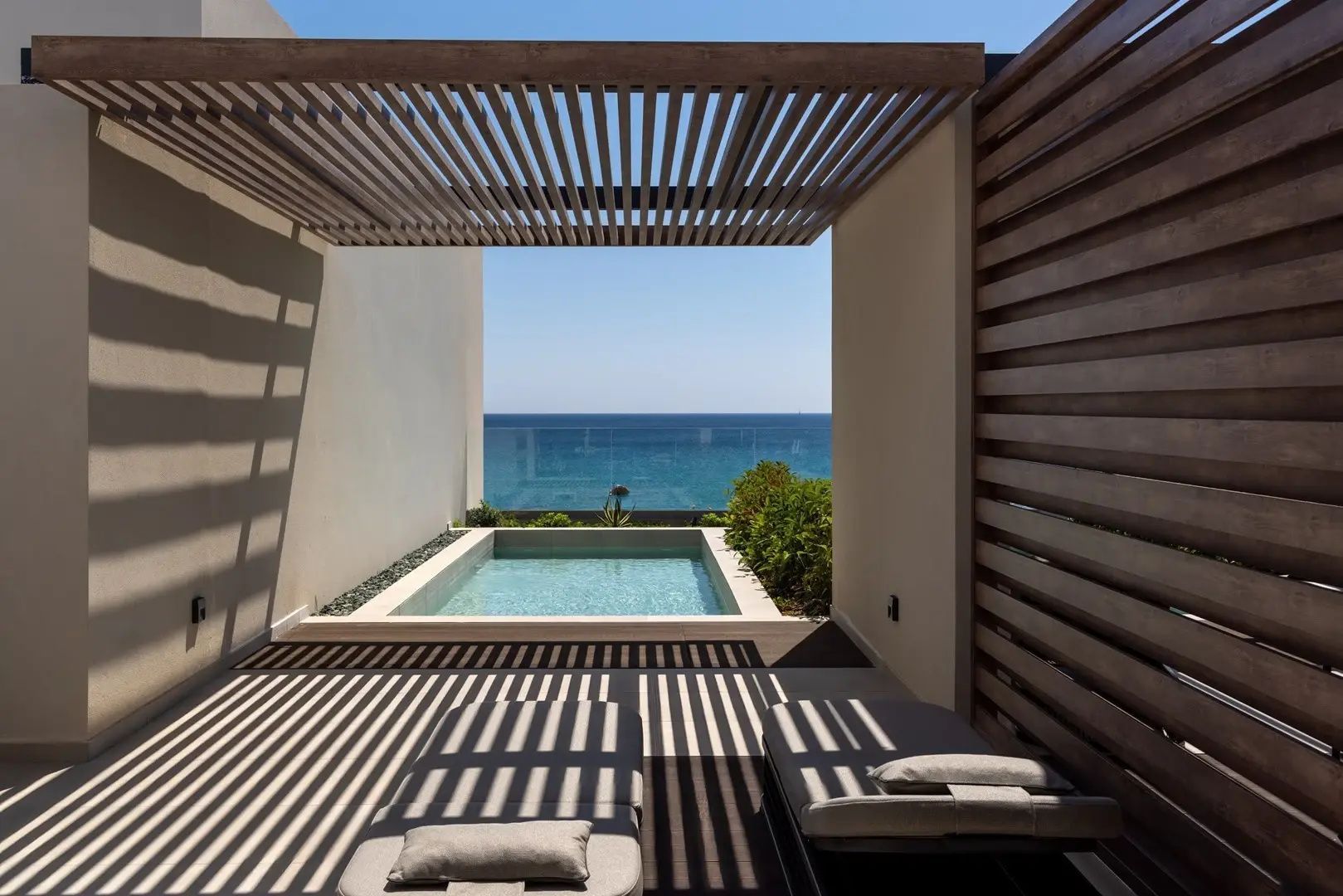 Sonnenterrasse mit Holzpergola, zwei Liegen, privatem Pool und direktem Blick auf das blaue Meer.