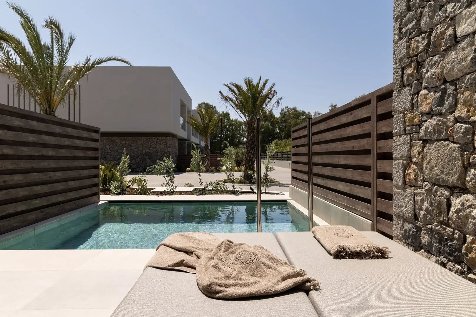 Sonnenterrasse mit privatem Pool, gepolsterten Liegen und Blick auf das Hotelgelände.