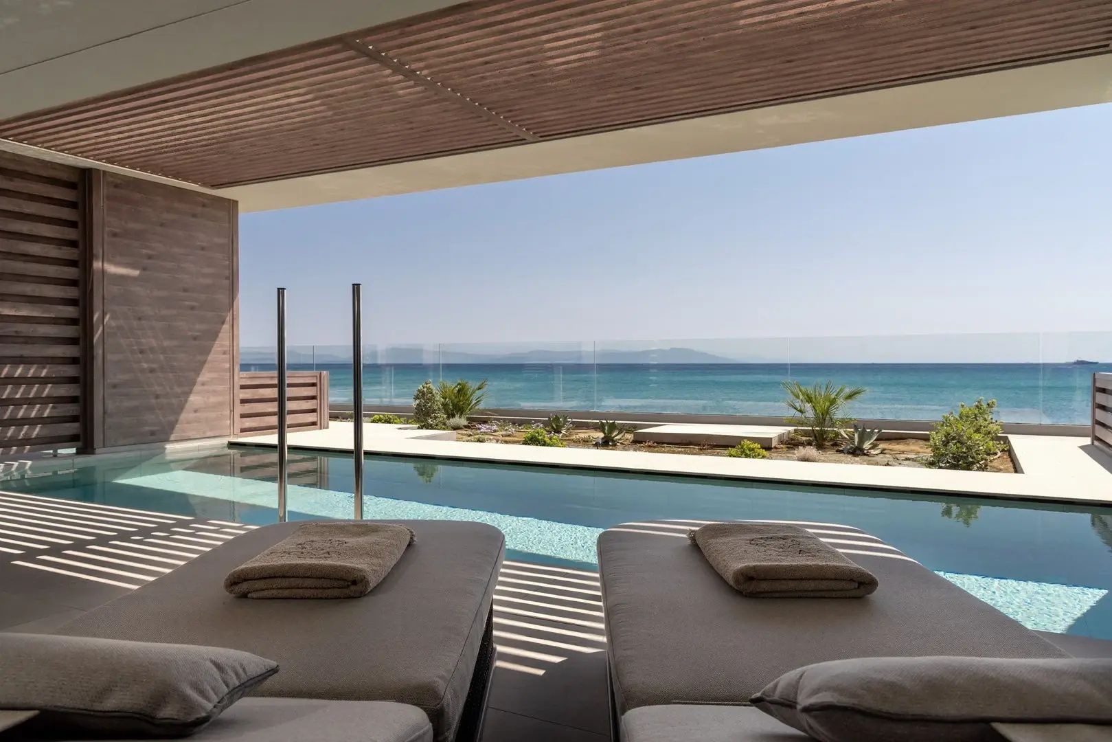 Zwei Liegen auf einer schattigen Terrasse mit eigenem Pool und Blick auf das Meer.
