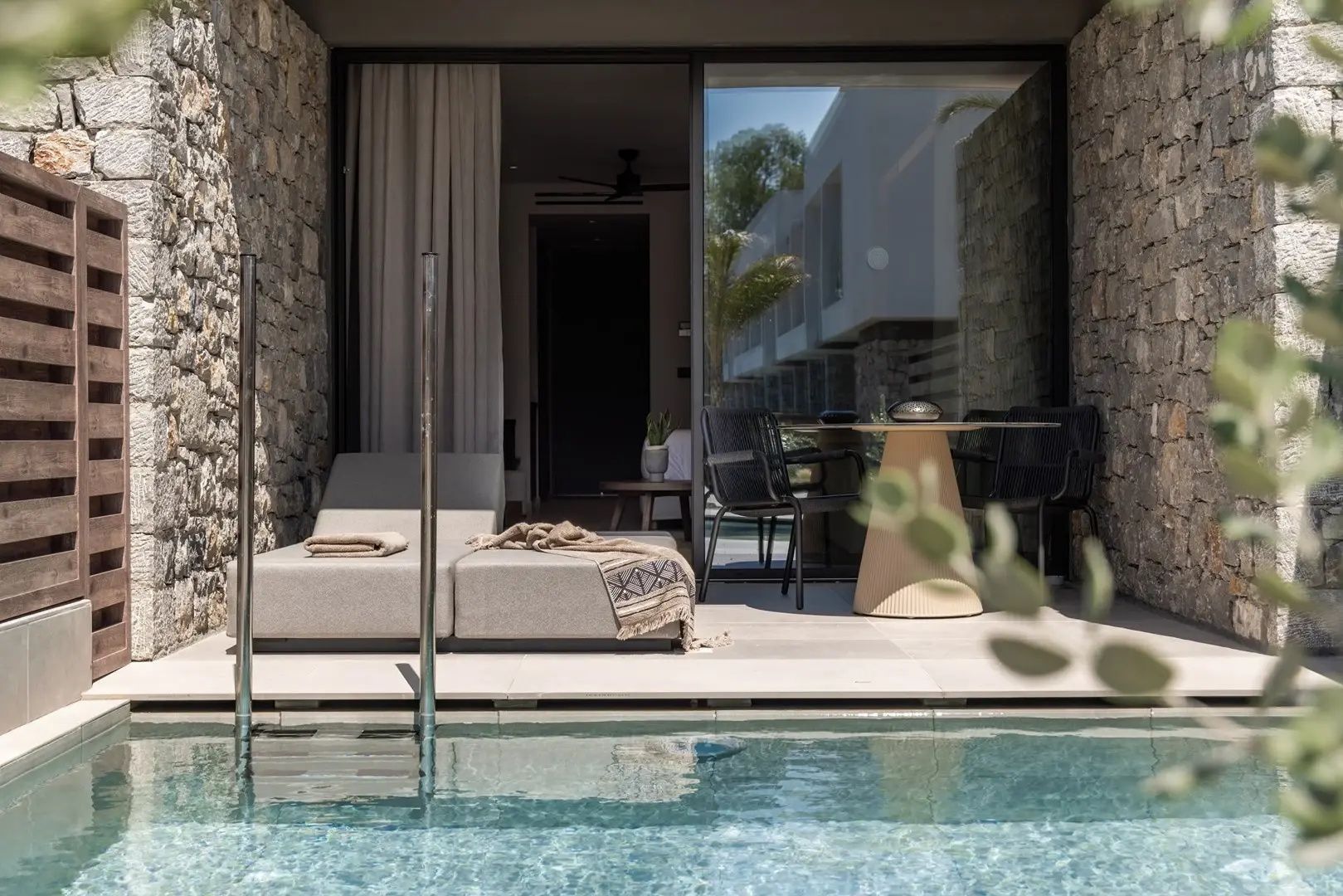Terrassenbereich mit direktem Poolzugang, Liege und Tisch mit Stühlen vor der Suite.