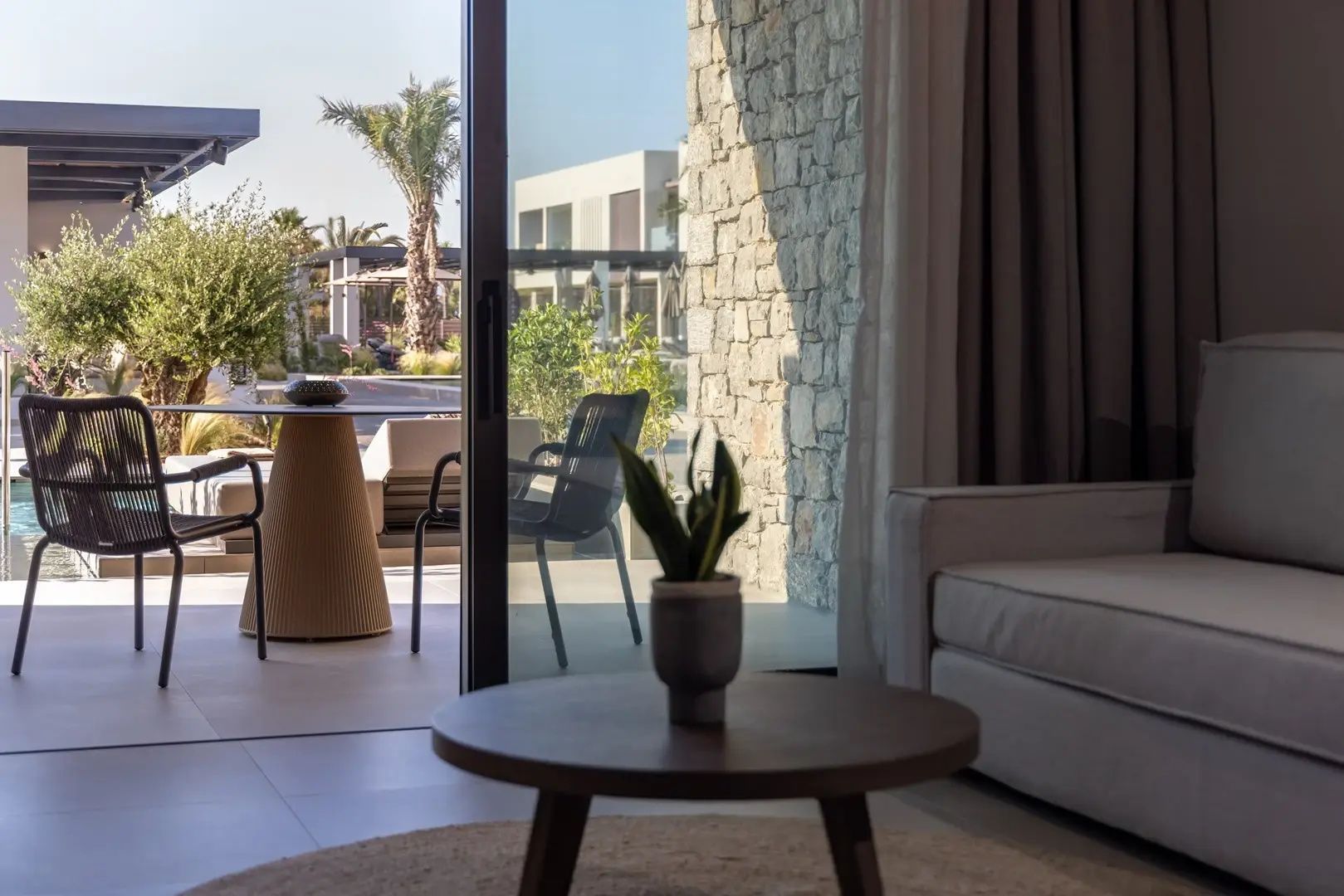 Blick aus dem Zimmer auf die möblierte Terrasse mit Natursteinwand und Außenbereich.
